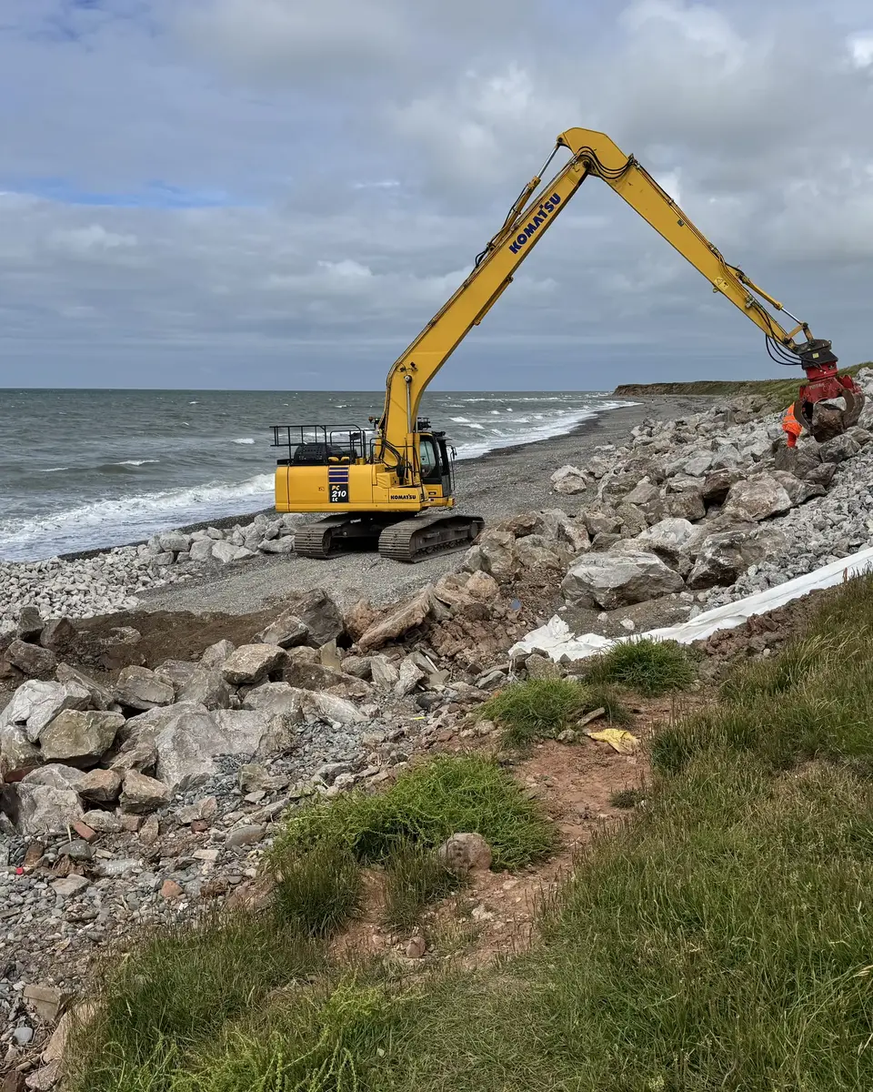 Portrait view of Cowran Estate Services excavator placing rock armour and liner beside the sea at South Walney