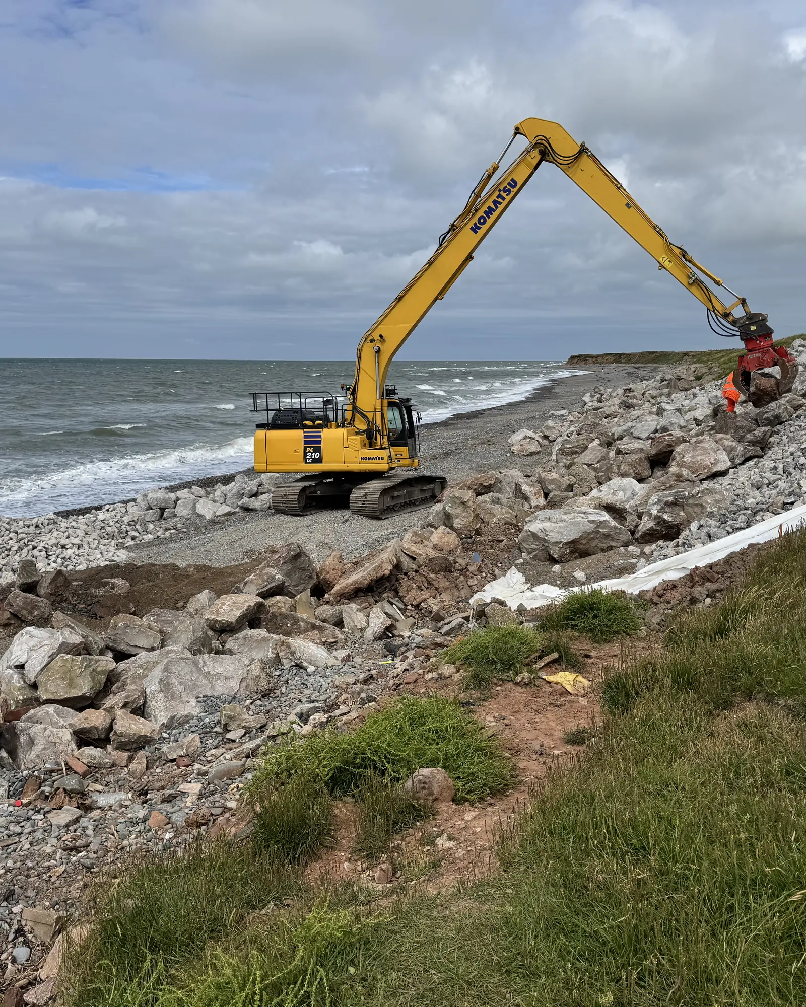 Portrait view of Cowran Estate Services excavator placing rock armour and liner beside the sea at South Walney
