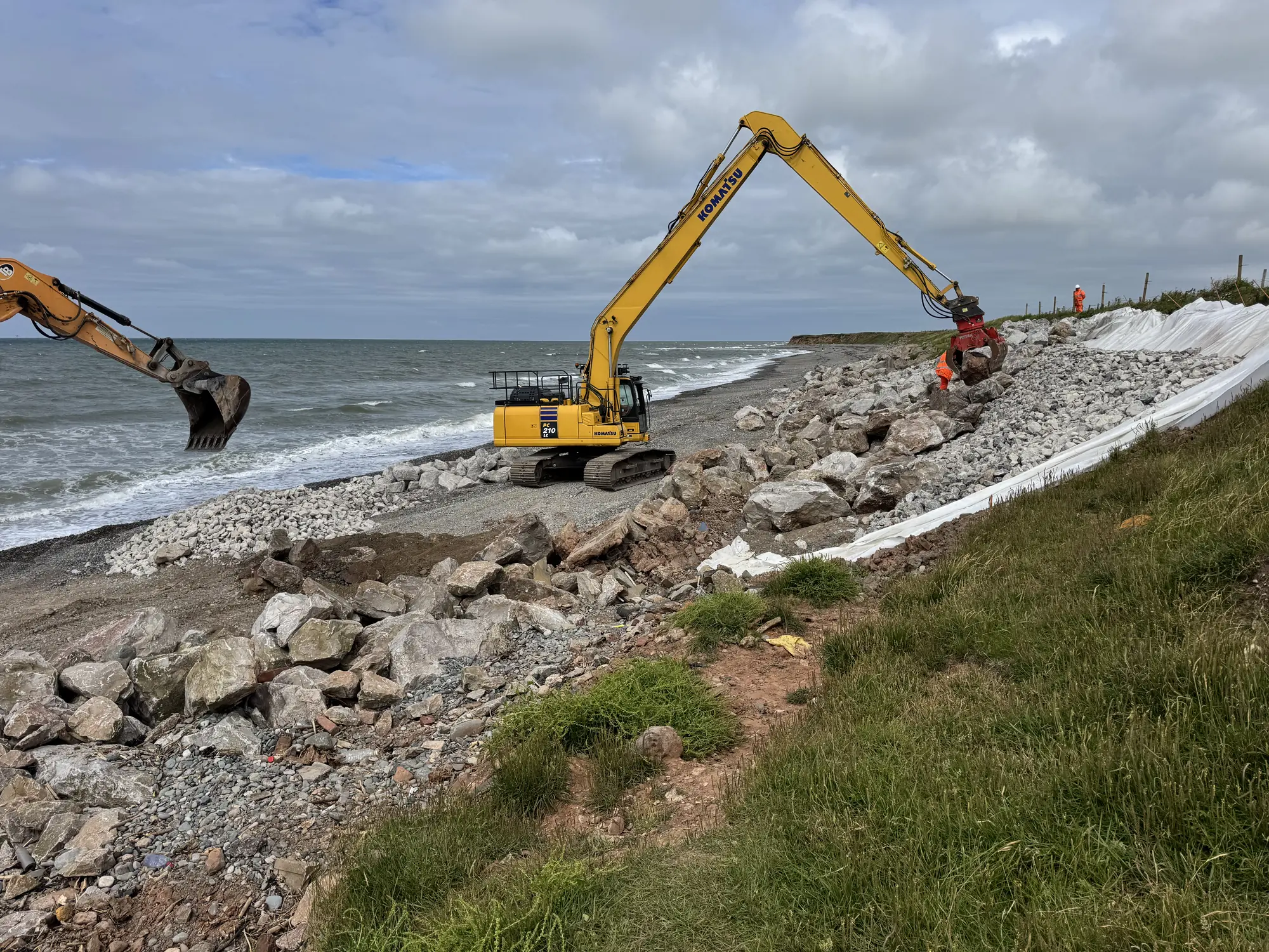 Close view of Cowran Estate Services excavator handling rock armour beside the geosynthetic liner on the South Walney coastal defence