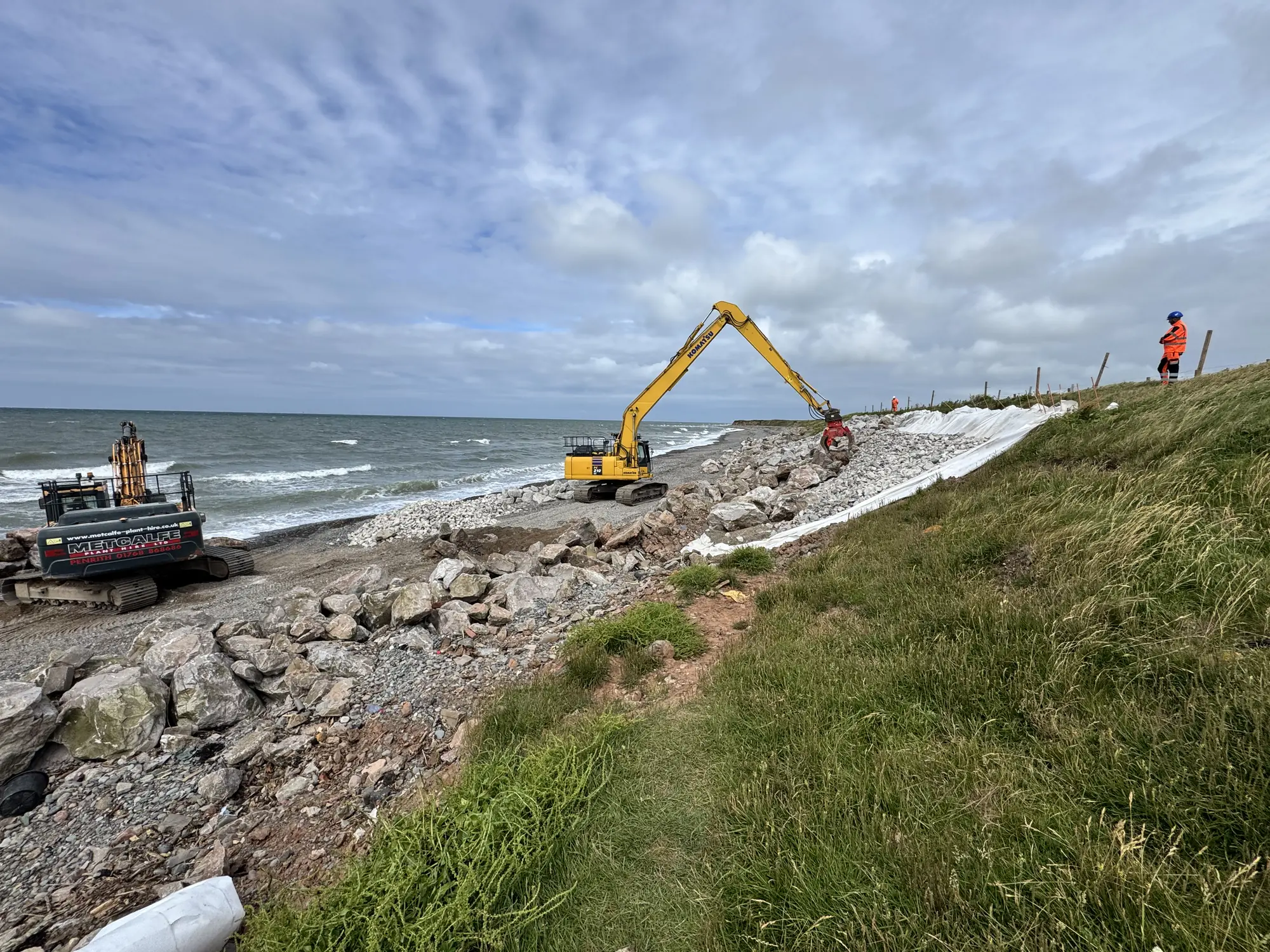 Cowran Estate Services excavator placing rock armour and liner beside the sea at South Walney